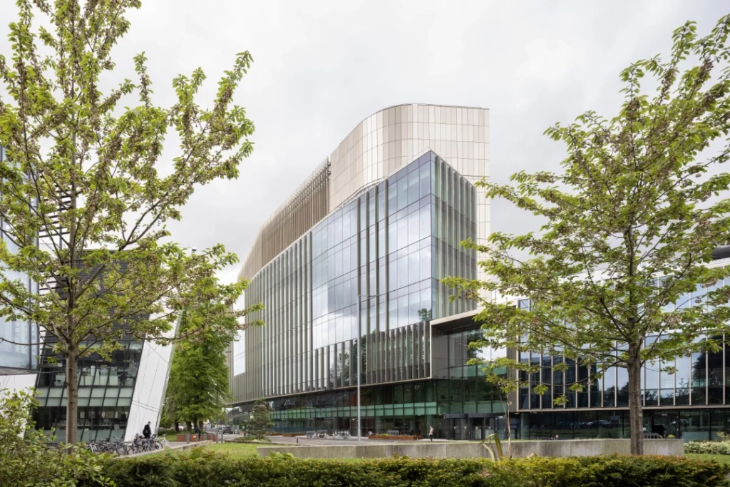 A photograph of the Paterson Building with bright green trees on either side, and the Oglesby Cancer Research Building on the left