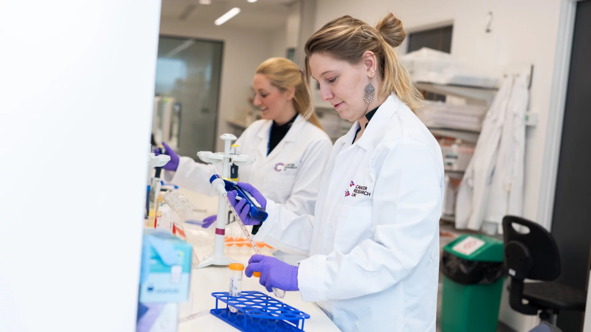 Researchers wearing lab coats and purple gloves working at a laboratory bench in the Paterson Building labs