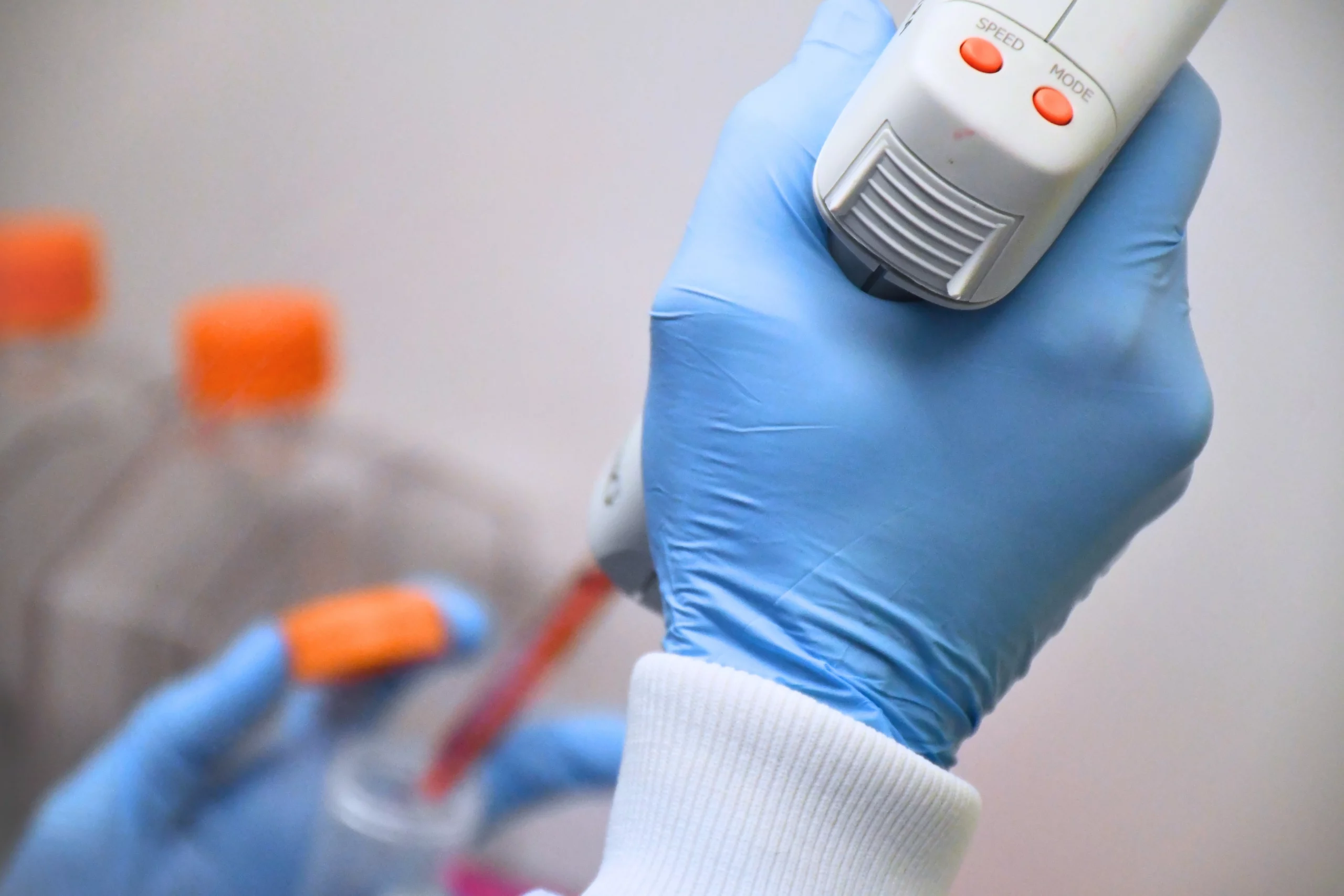 Gloved hands using pipette gun in tissue culture white lab coat